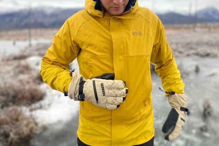 A man unzips his jacket while wearing gloves.