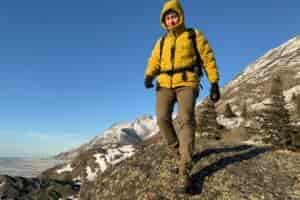 A man walks down a rocky ridge over an ocean view in the winter.