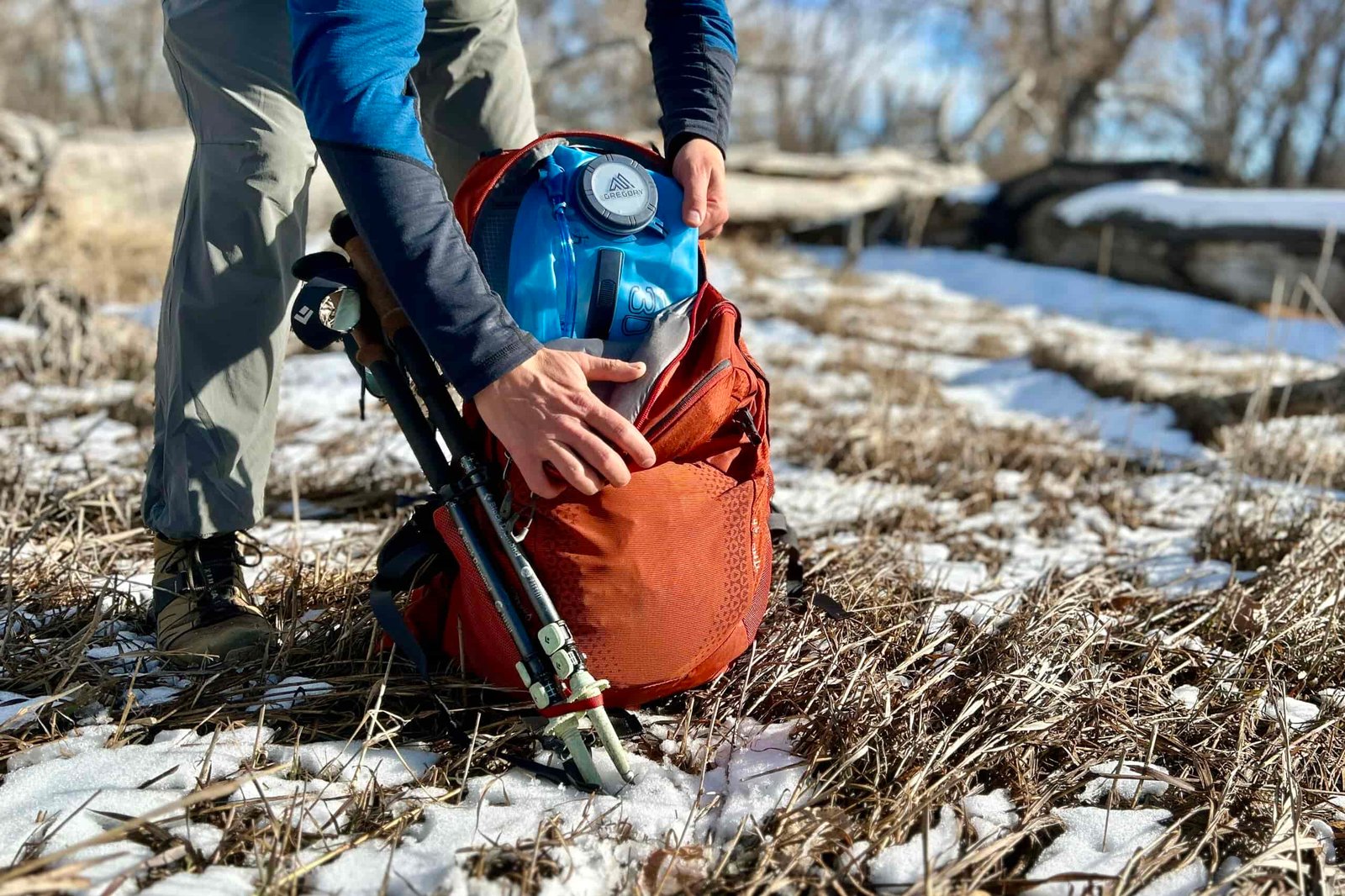 A person pulls the water reservoir out of their backpack, which is on the ground.