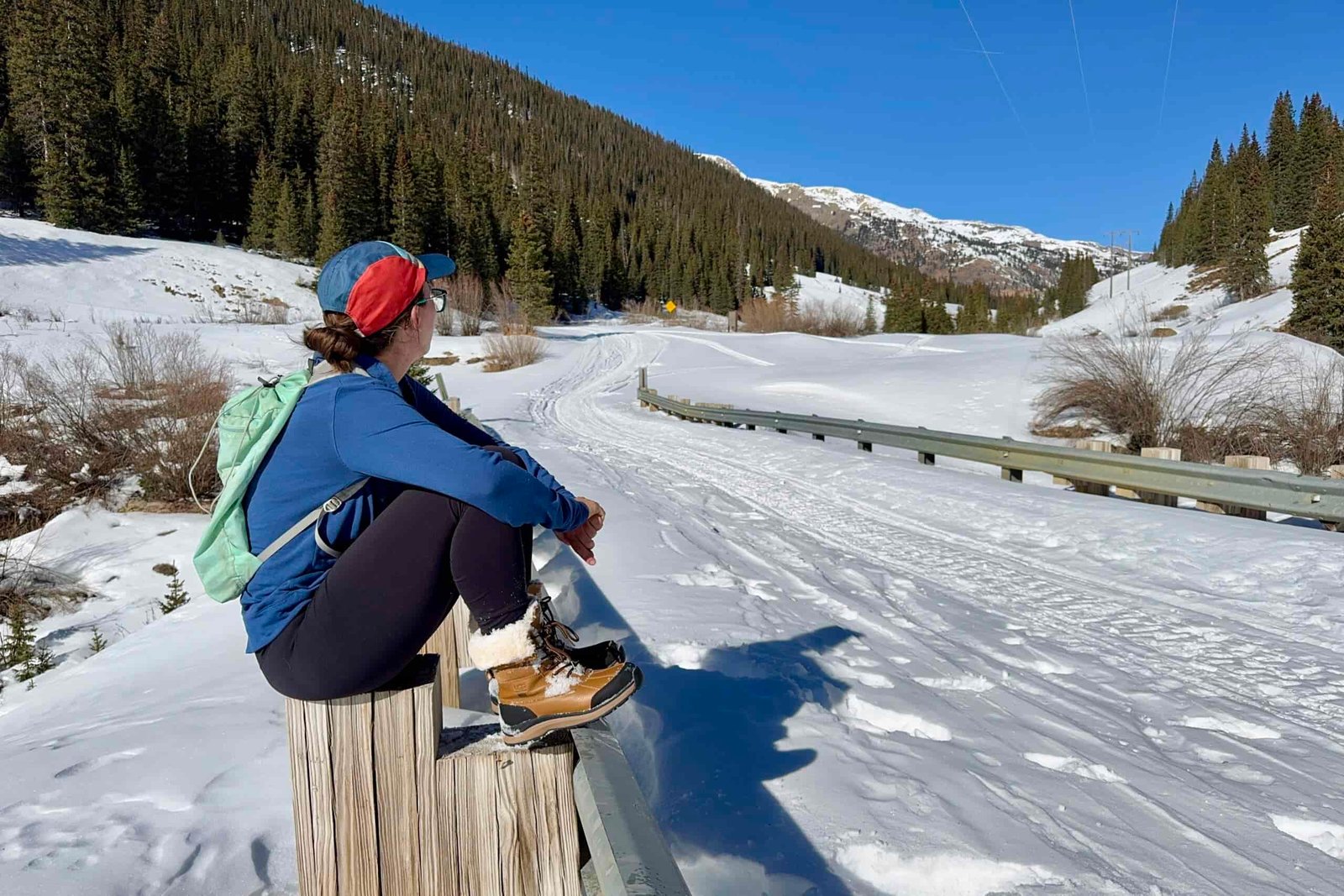 A person wearing the UGG boots is sitting on a rail looking at a mountain view.