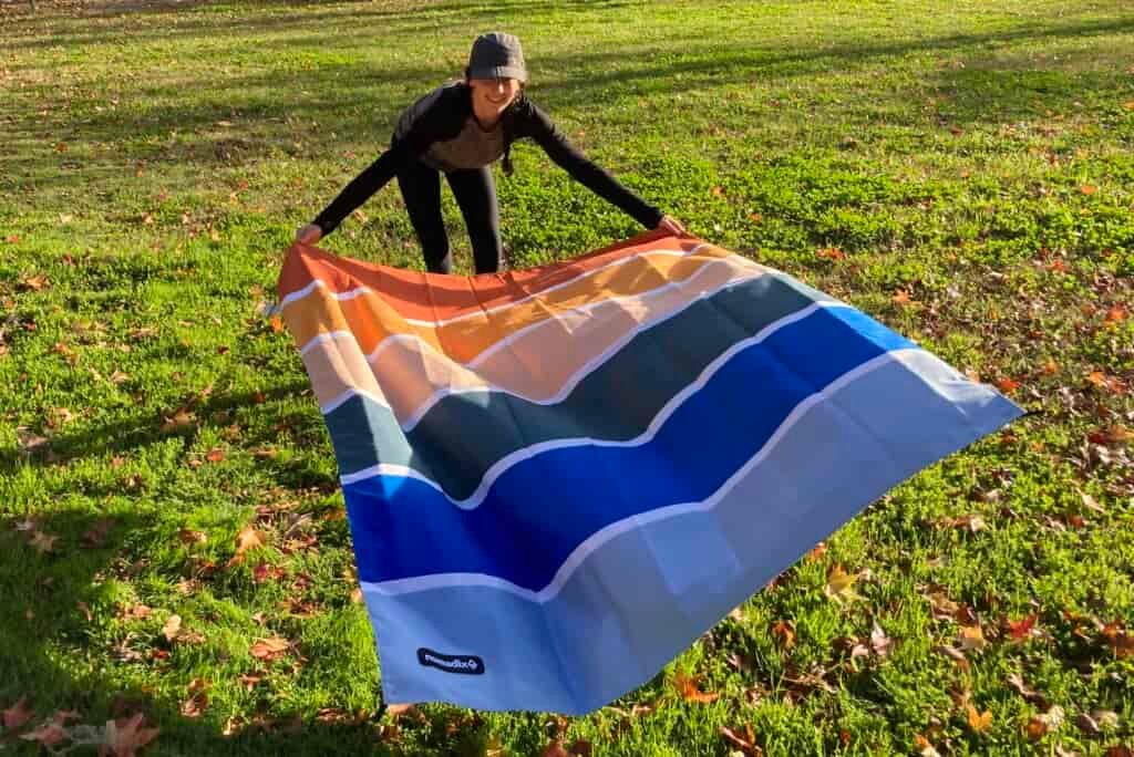 Women laying out the Nomadix Festival Blanket on a patch of grass