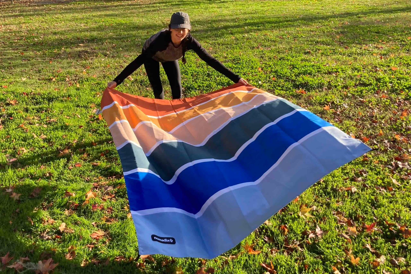 Women laying out the Nomadix Festival Blanket on a patch of grass