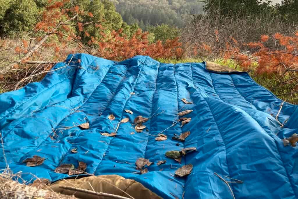 The REI camp blanket laid out on the ground covered in debris.