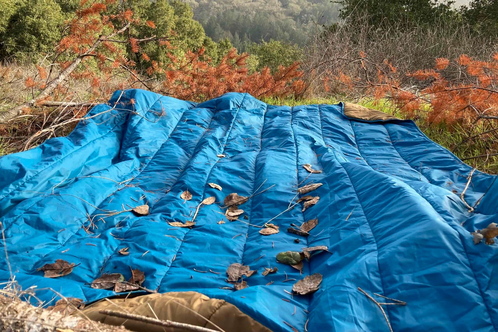 The REI camp blanket laid out on the ground covered in debris.