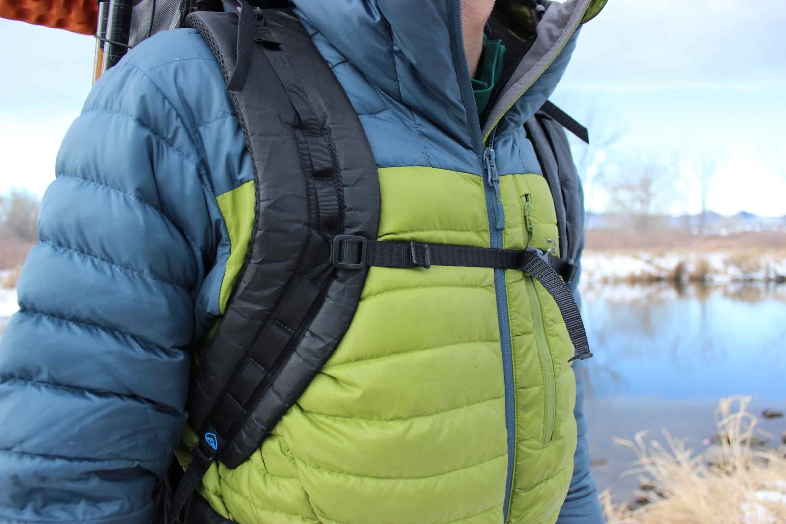 A close up of shoulder straps on a backpack worn by a hiker with water in the background.