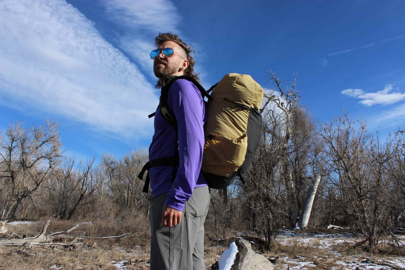 A hiker wears the pa'lante v2 backpack with trees and blue skies in the background.