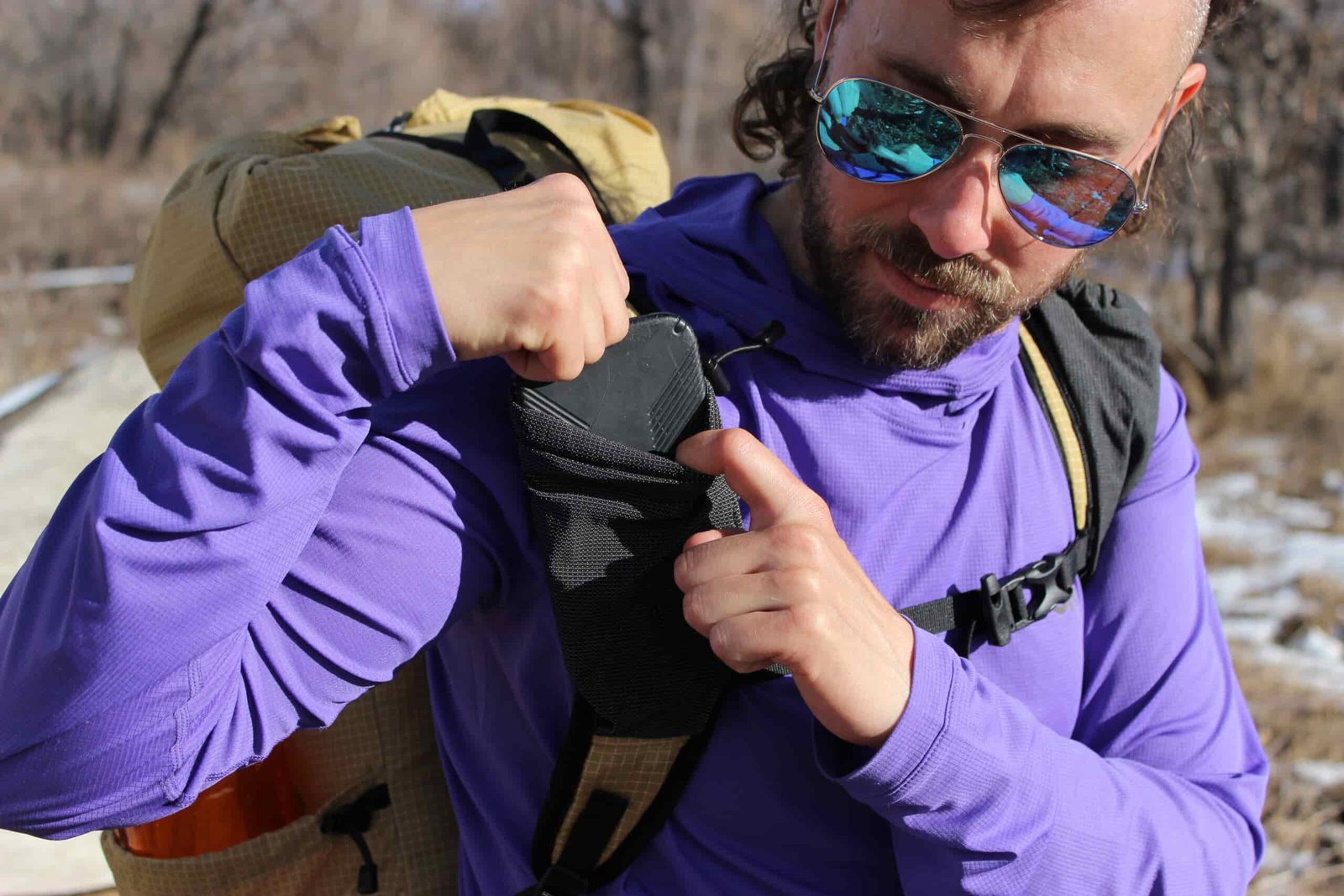 A hiker pulls a smartphone out of the shoulder strap pocket of the Pa'Lante V2.