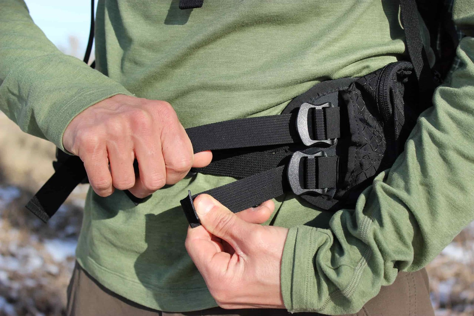 A hiker pulls on the hipbelt adjustments of a backpack.