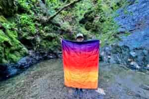 Person holding up the Rumpl NanoLoft Puffy Blanket with a mossy wooded background, to compare blanket size to the person’s height.