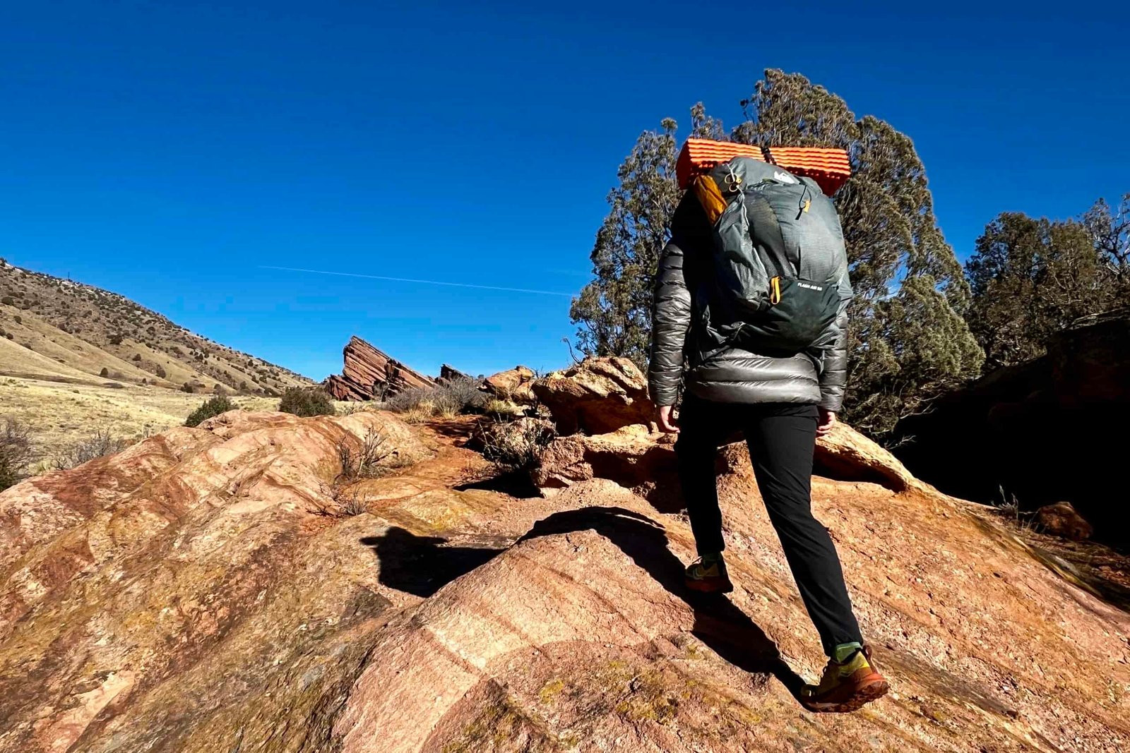 A hiker walks up a red rock formation while wearing a grey backpack.