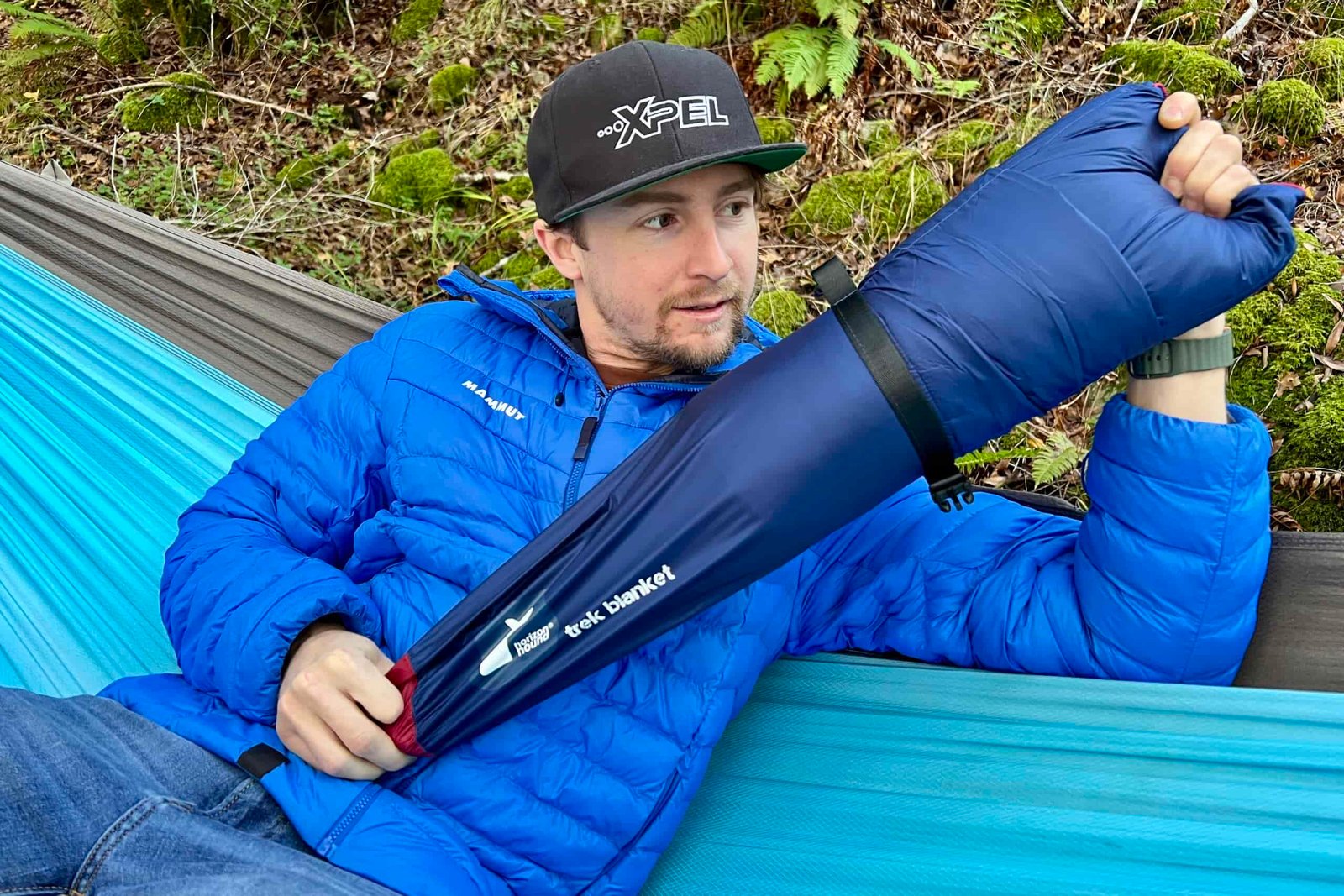Man sitting in a hammock, pulling the Horizon Hound Trek Blanket out of its carry case.