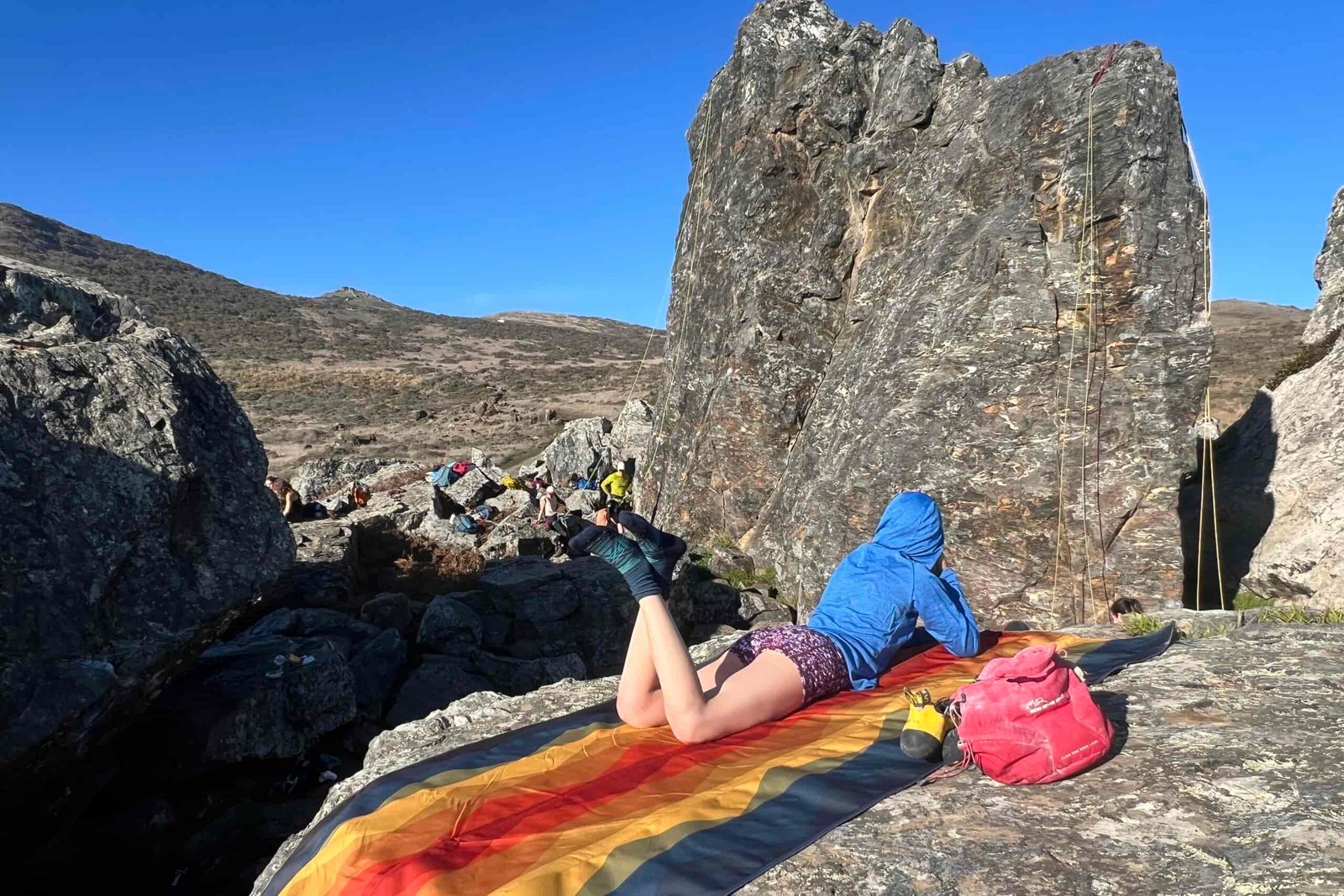 Woman laying out on the Nemo Victory Patio Blanket in front of a rock climbing scene.