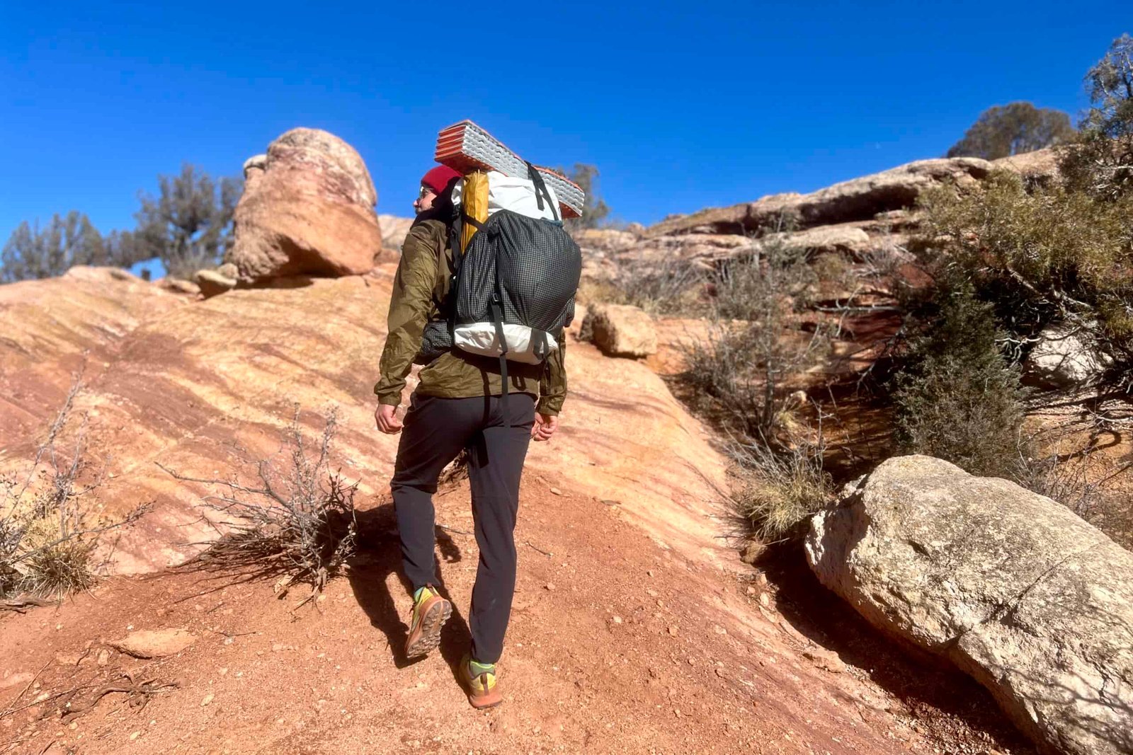 A hiker walking on red rocks while wearing the HMG Southwest 55 pack and a desert background