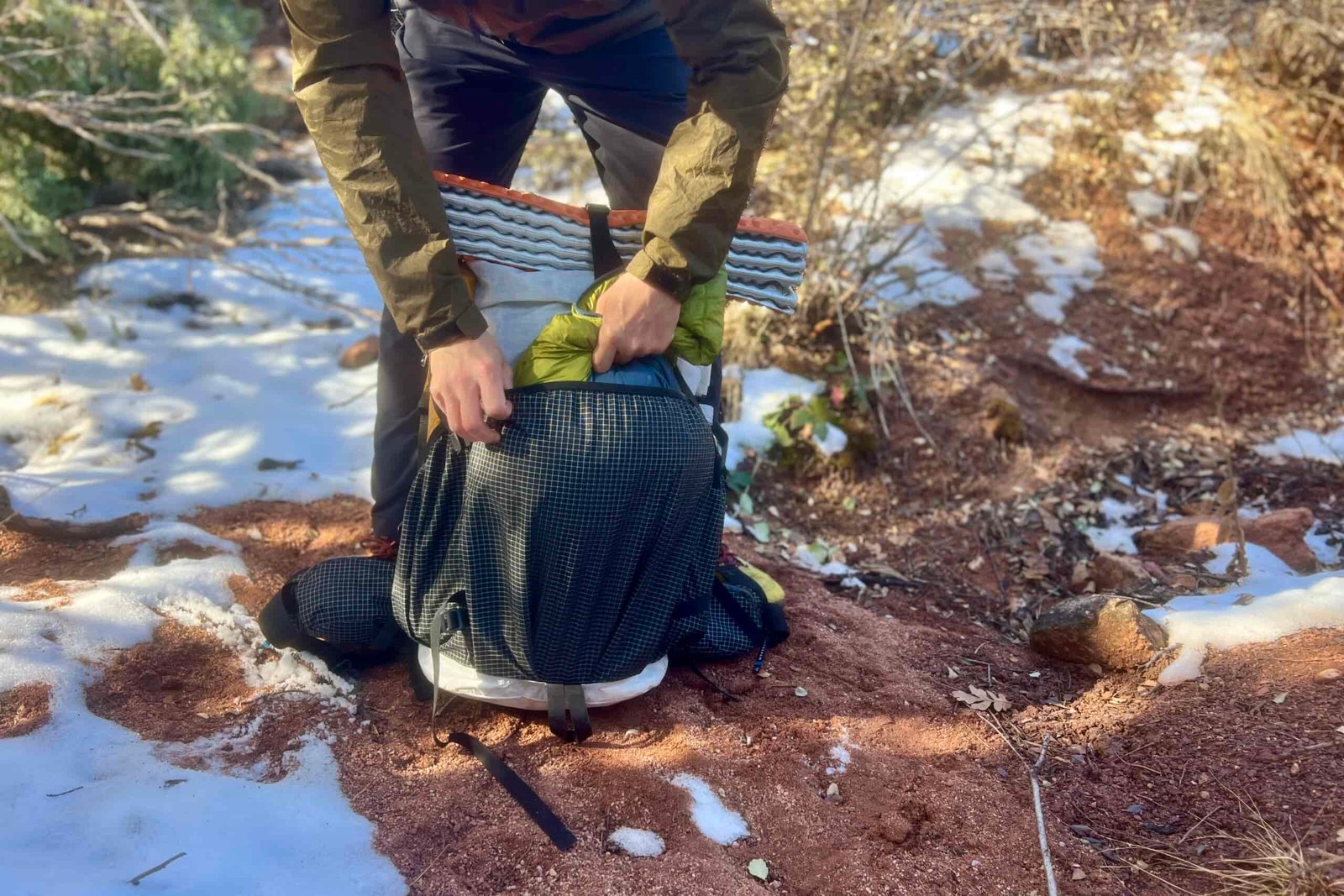 I hiker pulls a puffy jacket from the front pocket on the Southwest 55 pack with a snowy desert background.