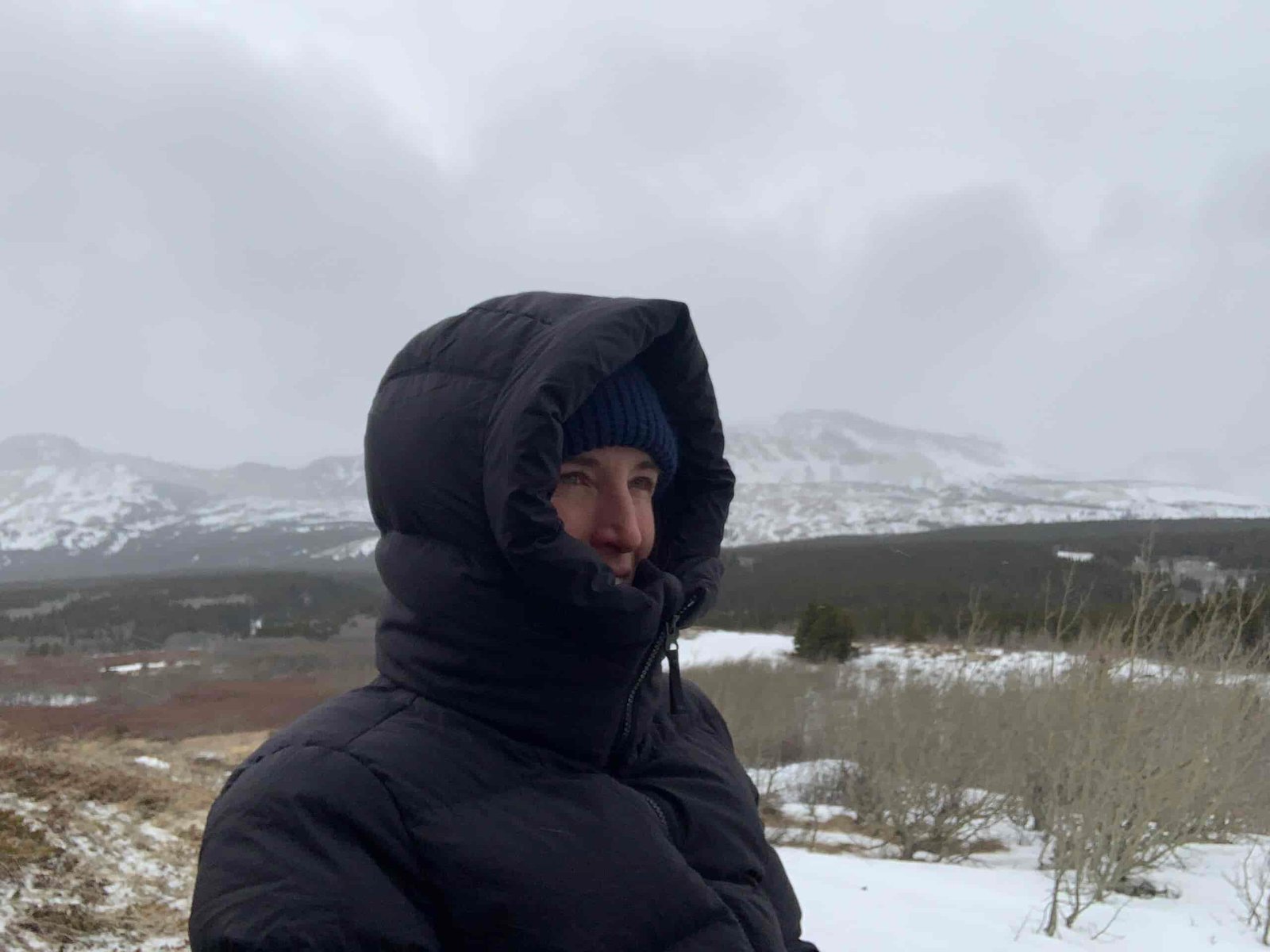 A woman wearing the Outdoor Research Coze Down parka with the hood on to showcase the down baffle ruff and tall collar