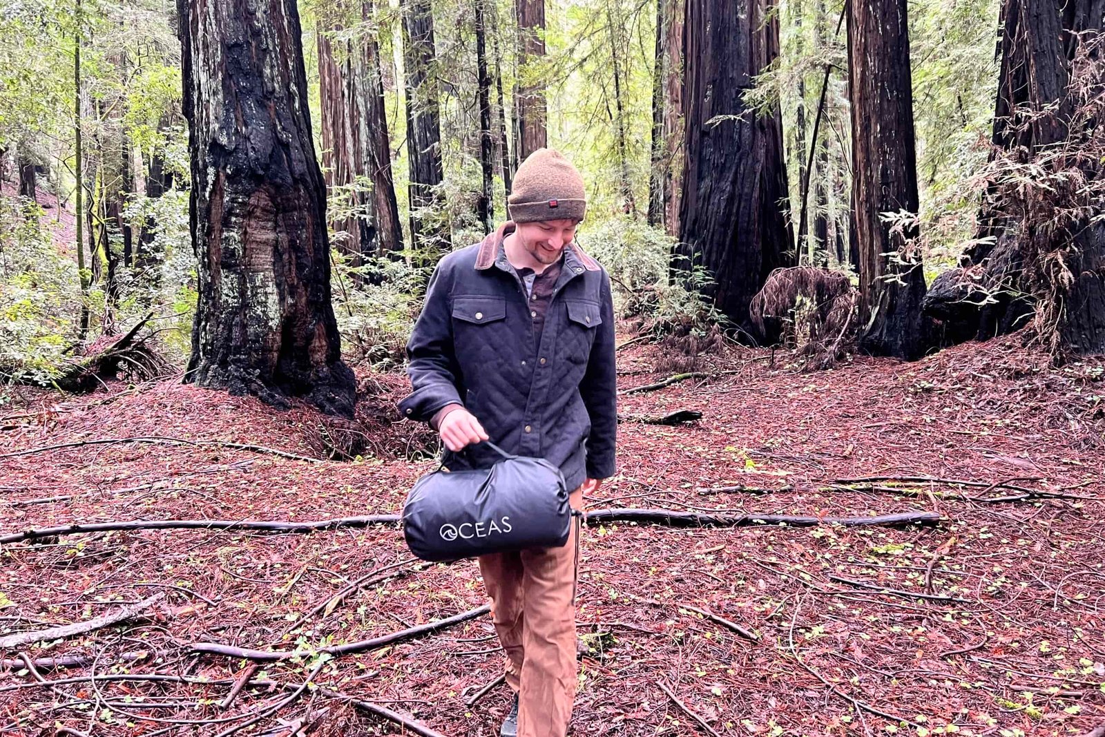 Man walking through the redwoods carrying the Oceas Sherpa Fleece Blanket by its handle.