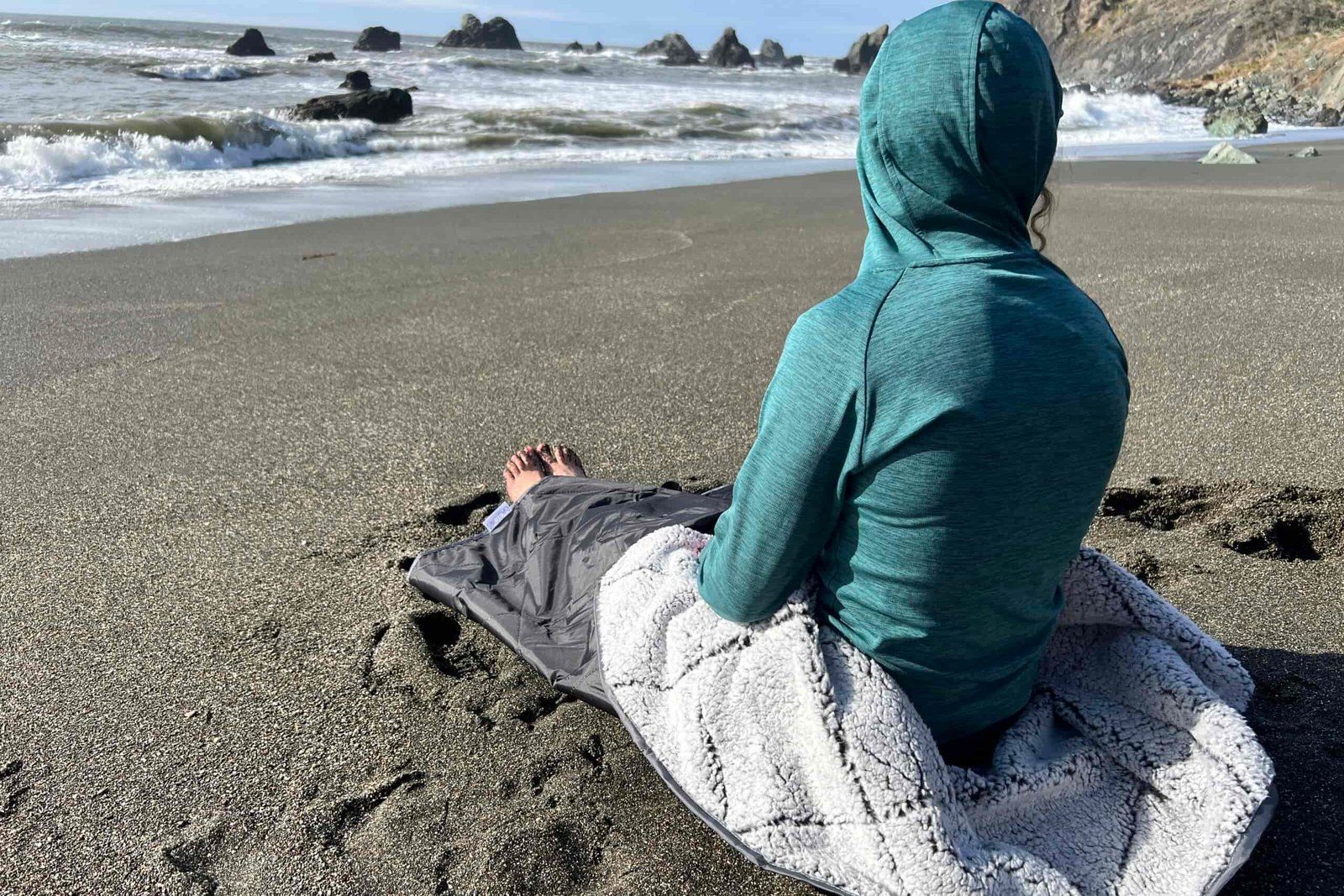 Women wrapped in the Oceas Sherpa Fleece Blanket while sitting on the beach.