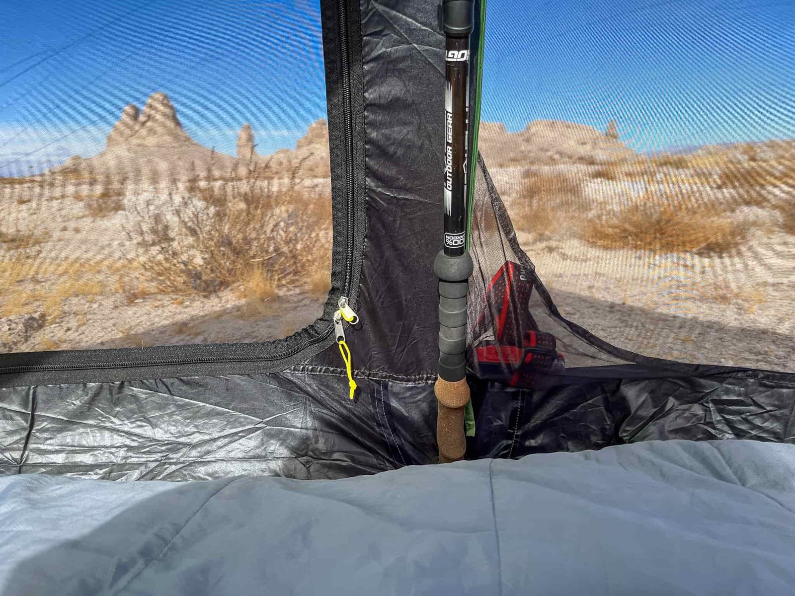 Closeup view of the interior mesh wall showing where the handle of a trekking pole rests in the reinforced support area. Also shows one of the sidewall pockets with a headlamp inside. Desert landscape visible outside in the distance.
