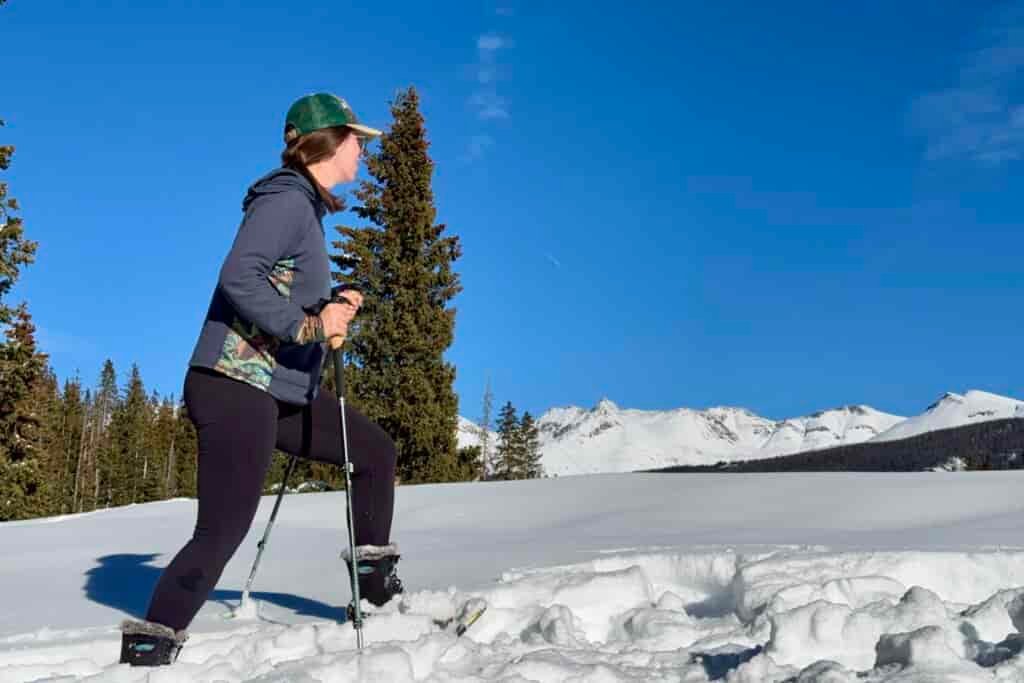 A person is snowshoeing through the snow while wearing the Bogs Arcata boots. There are mountains in the background.