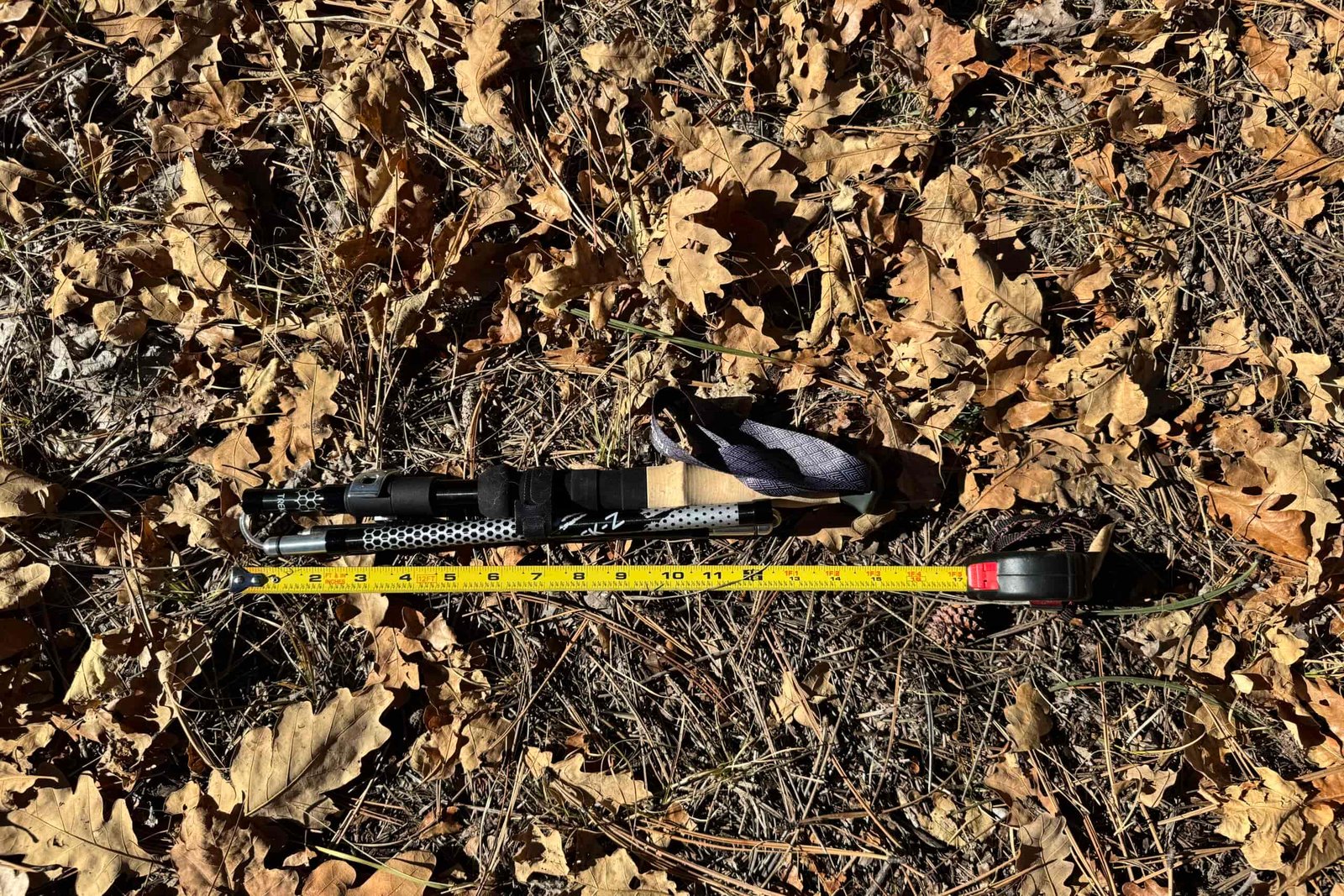 The Trekology Trek-Z 2.0 pole is laying on the ground in some leaves with a measuring tape next to it.