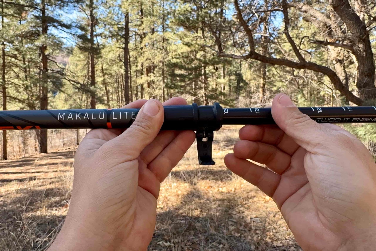 A close up of a hand closing a flick lock with trees in the background.