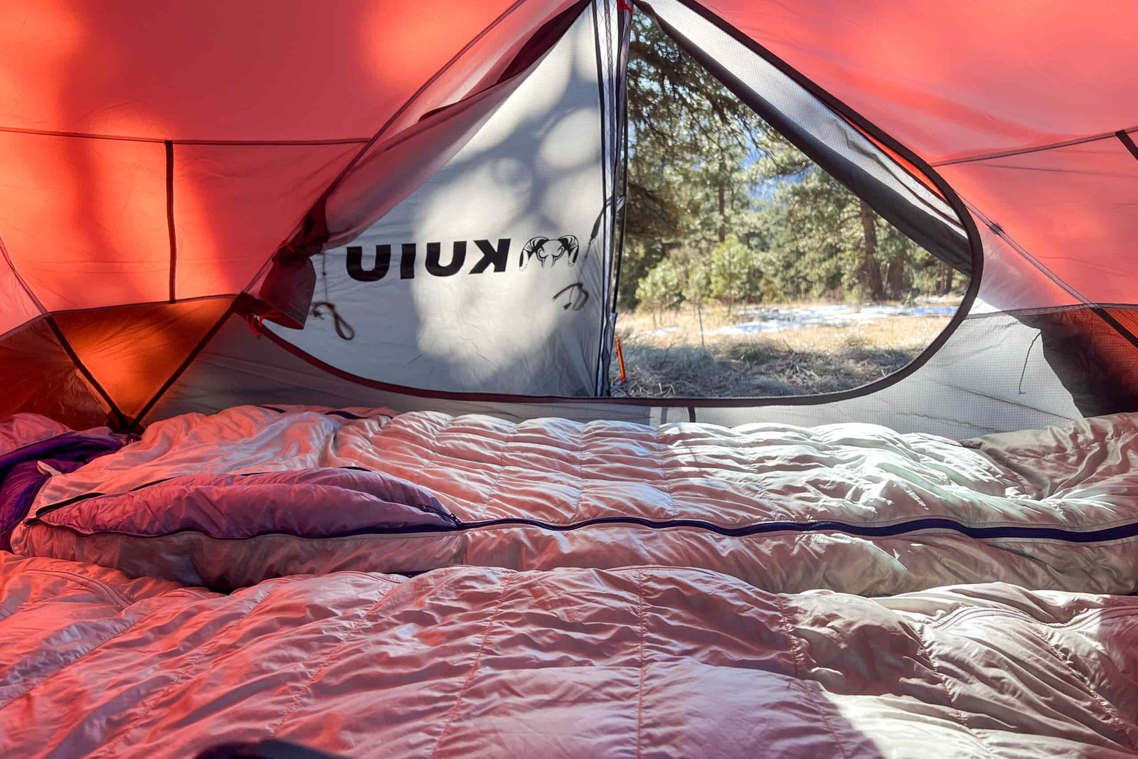 Inside view of the KUIU Storm Star 2P tent showing two sleeping bags and the open vestibule with a scenic outdoor background.