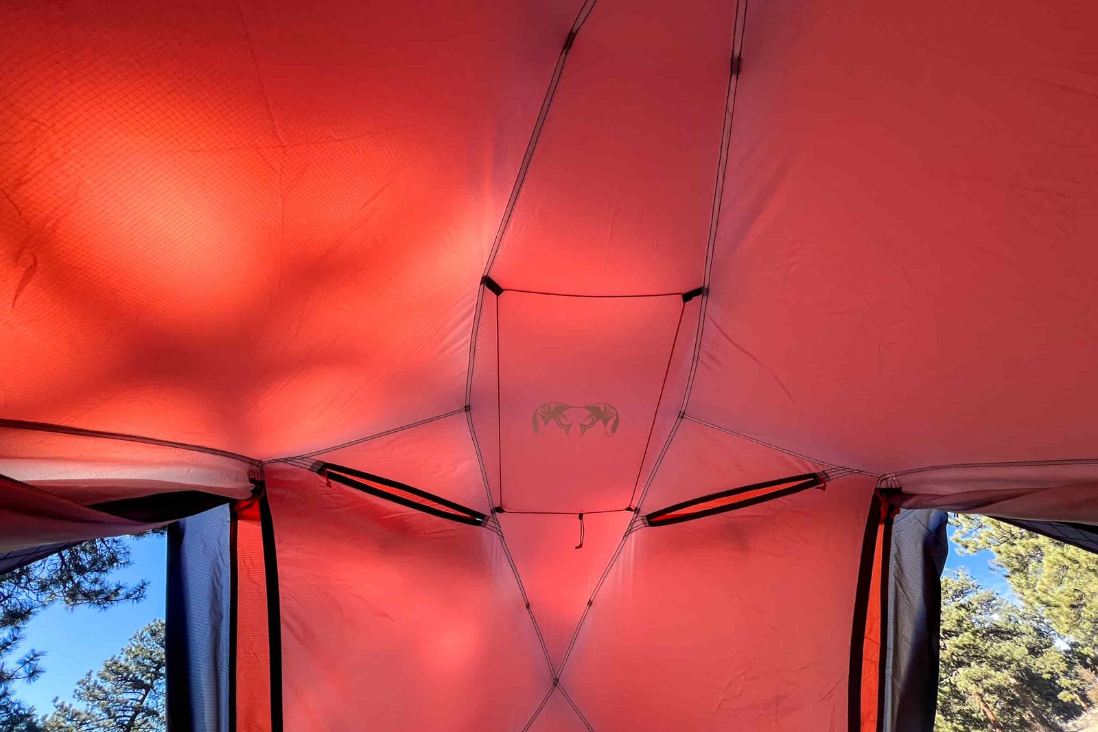 Interior view of the KUIU Storm Star 2 tent illuminated by red light, showcasing the ceiling's unique panel structure with storage pockets and the KUIU logo.