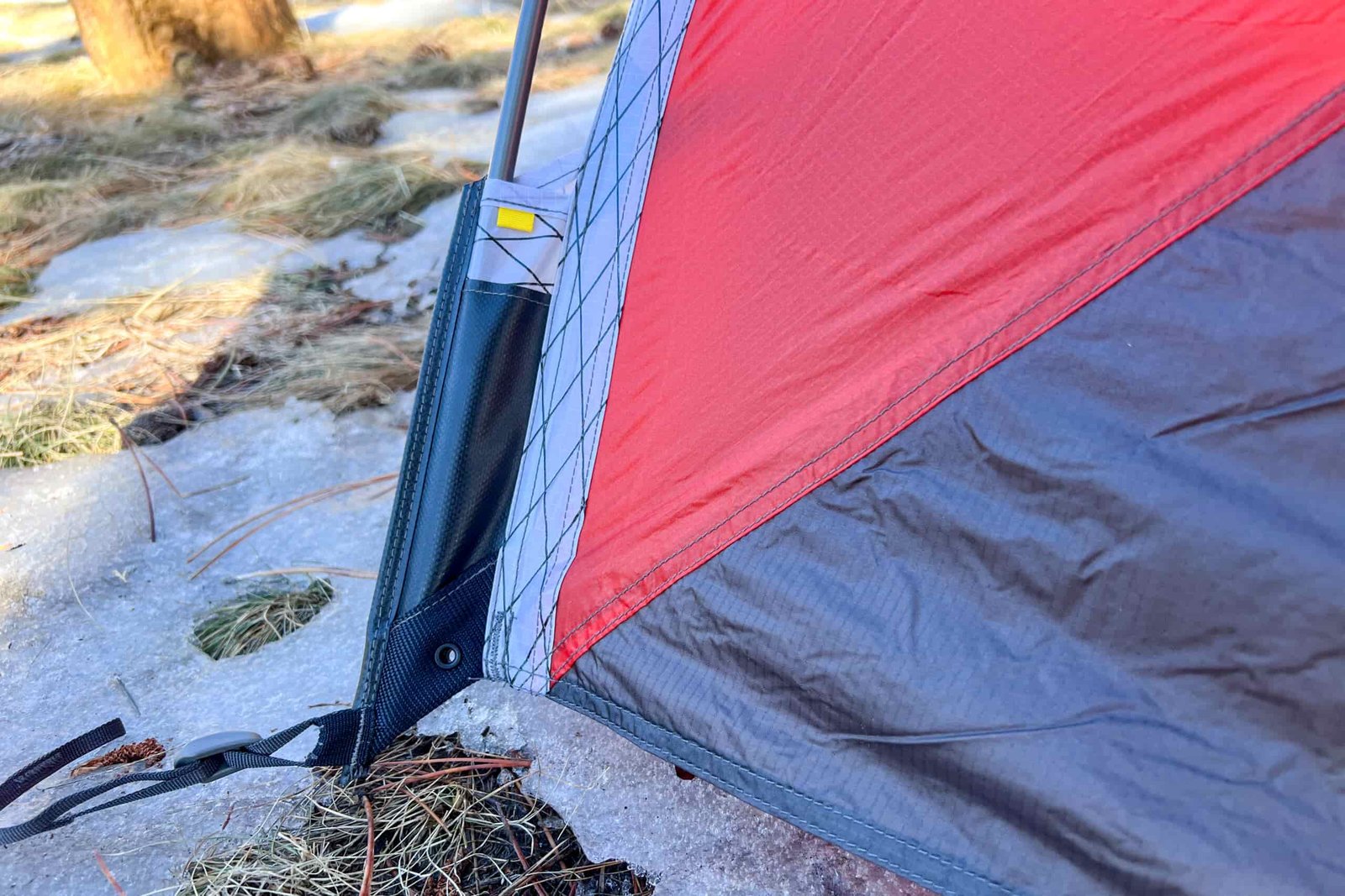 Close-up of a reinforced corner of the tent, showing durable stitching, a pole sleeve, and red fabric secured to the ground.