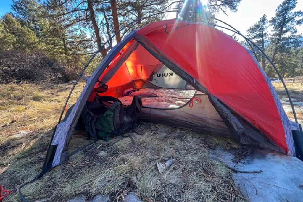 Side view of the KUIU Storm Star 2P tent with the vestibule open, showing gear and sleeping bags inside.