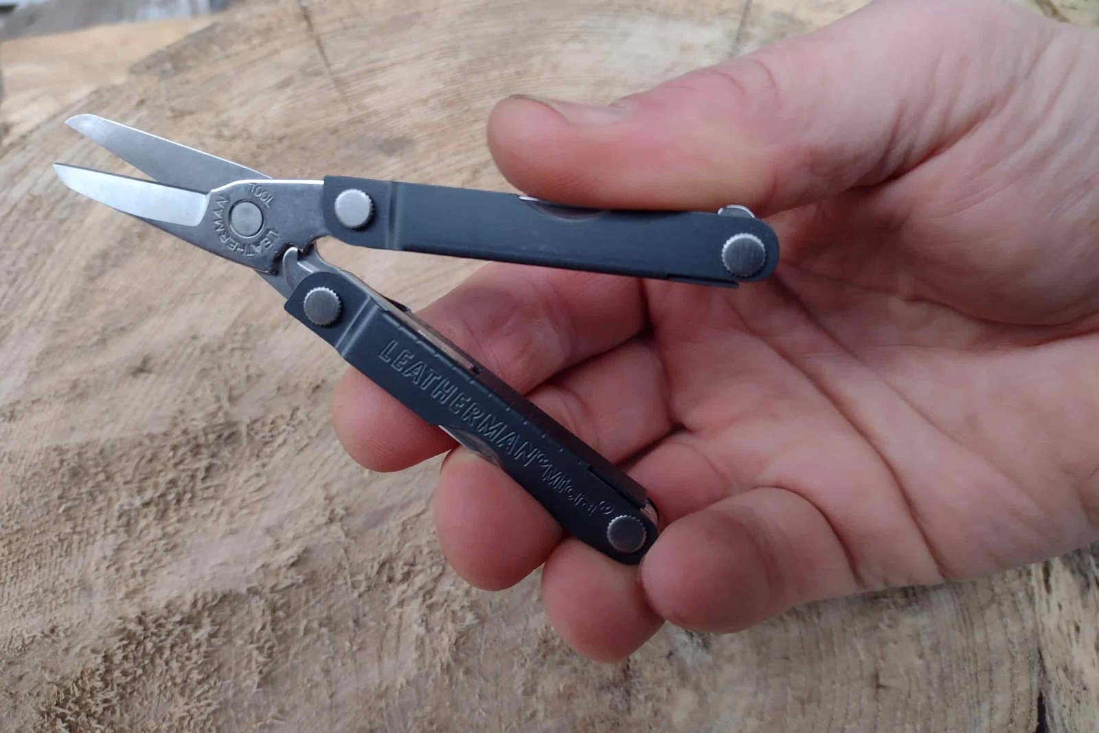 The Leatherman Micra in hand, held above a log.