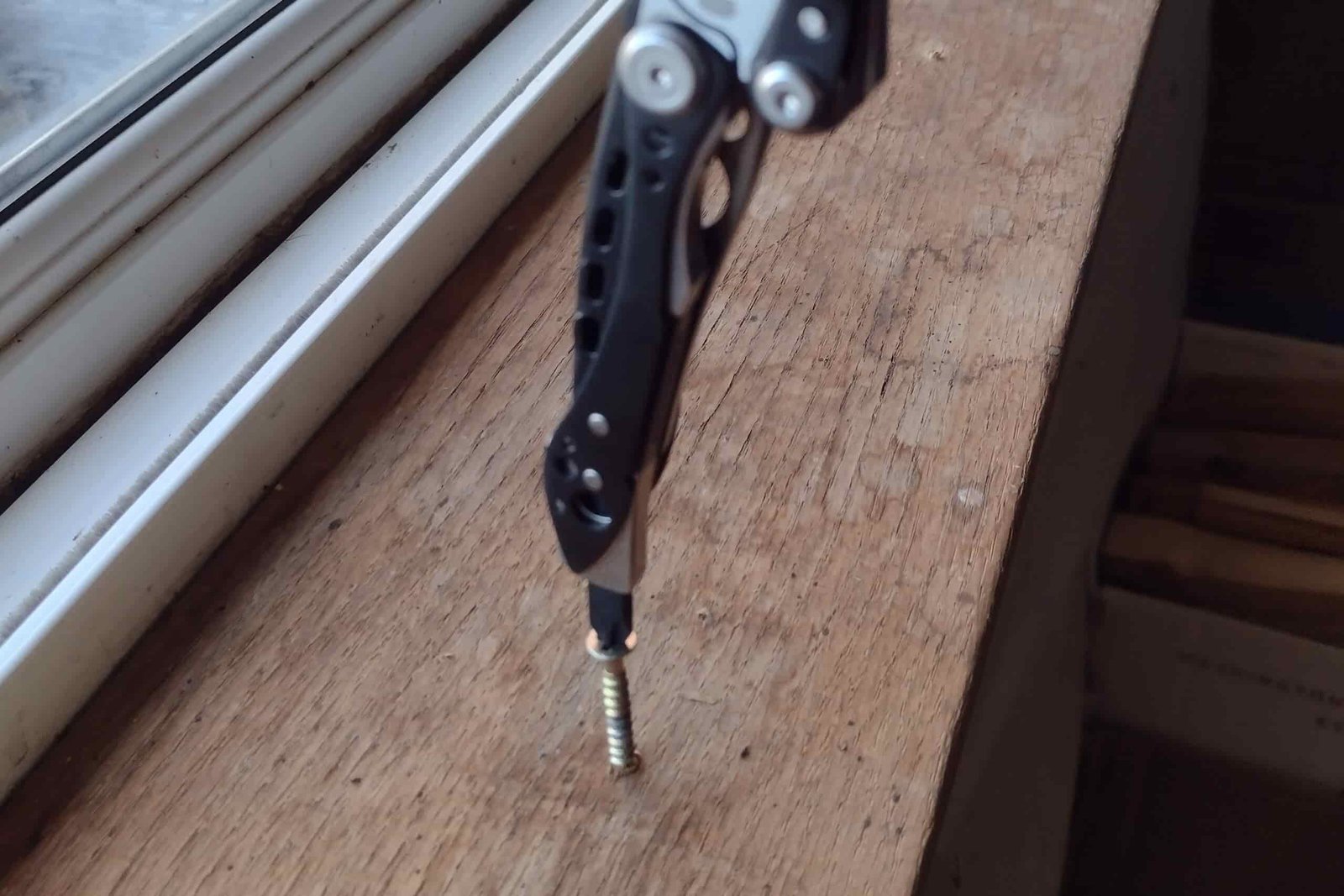 The Leatherman Skeletool CX in vertical position, turning in a Phillips screw into cedar trim board,