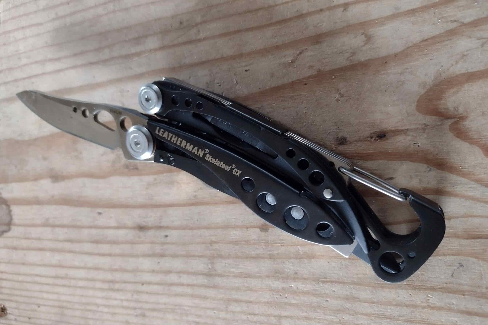 The Leatherman Skeletool CX resting on a board with its knife blade open.