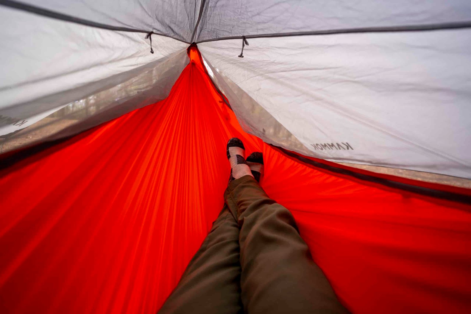 A pair of legs stretch out into an orange hammock from a point of view perspective