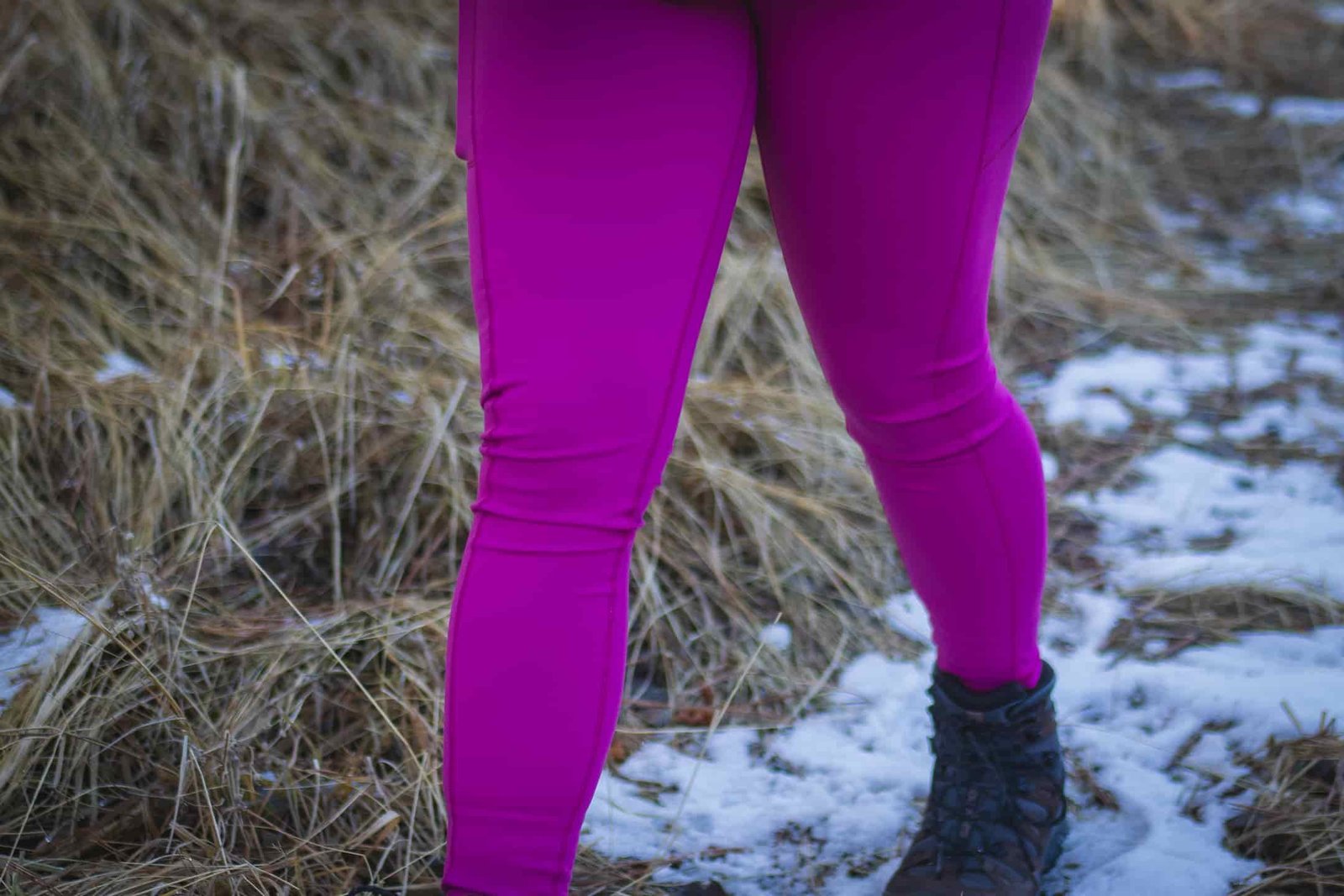Person hiking in bright pink leggings, wearing a bronze down jacket and black gloves.
