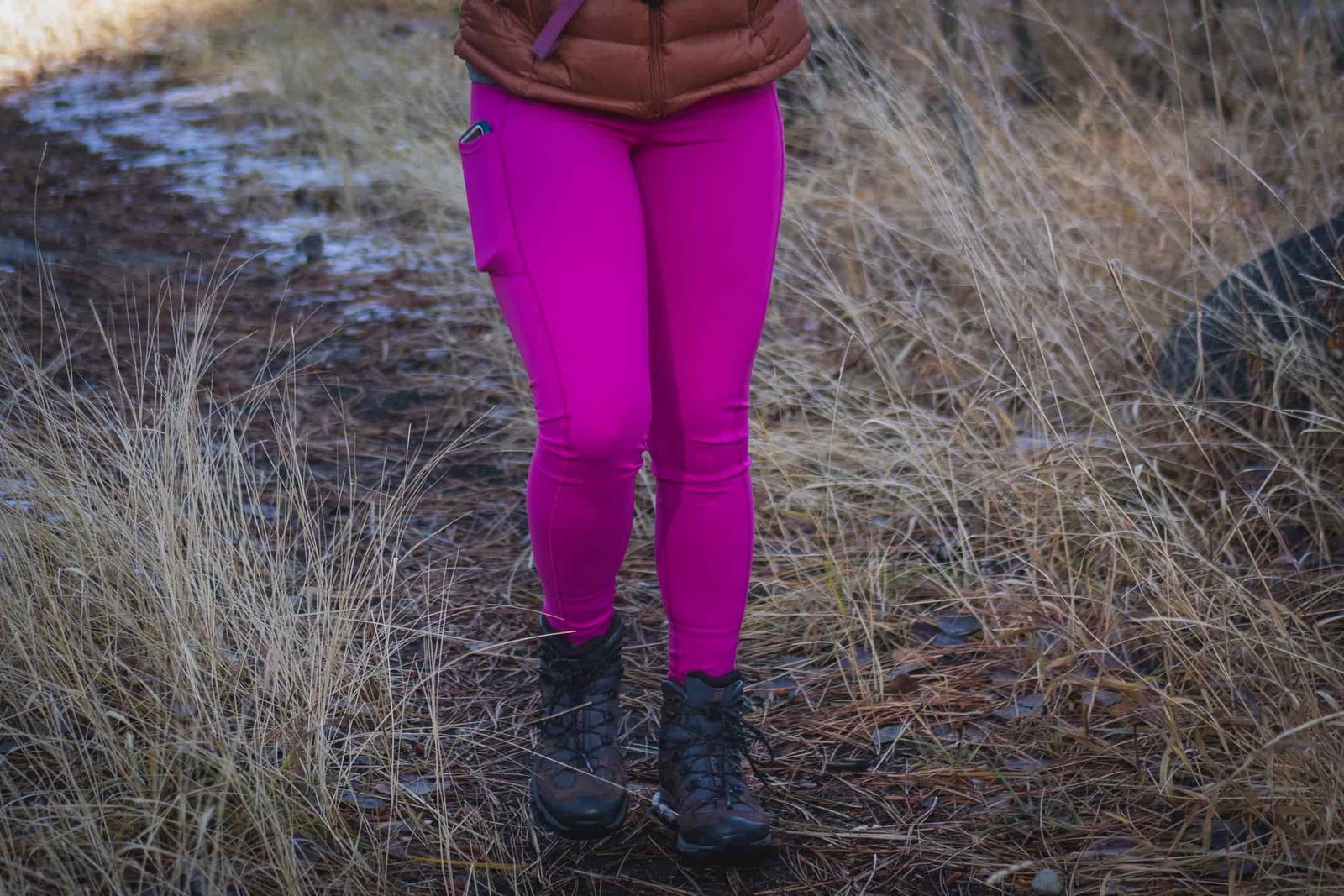 Person hiking in bright pink leggings, wearing a bronze down jacket and black gloves.
