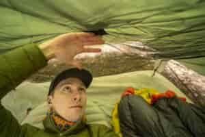 A man in a green jacket lays down in a tent
