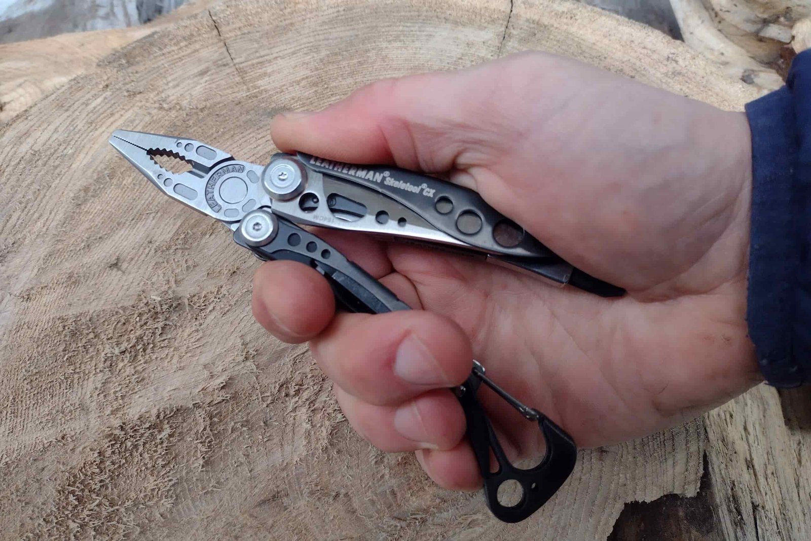 The Leatherman Skeletool CX held in hand above a log.