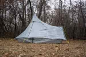 a silver green tent in a forest clearing