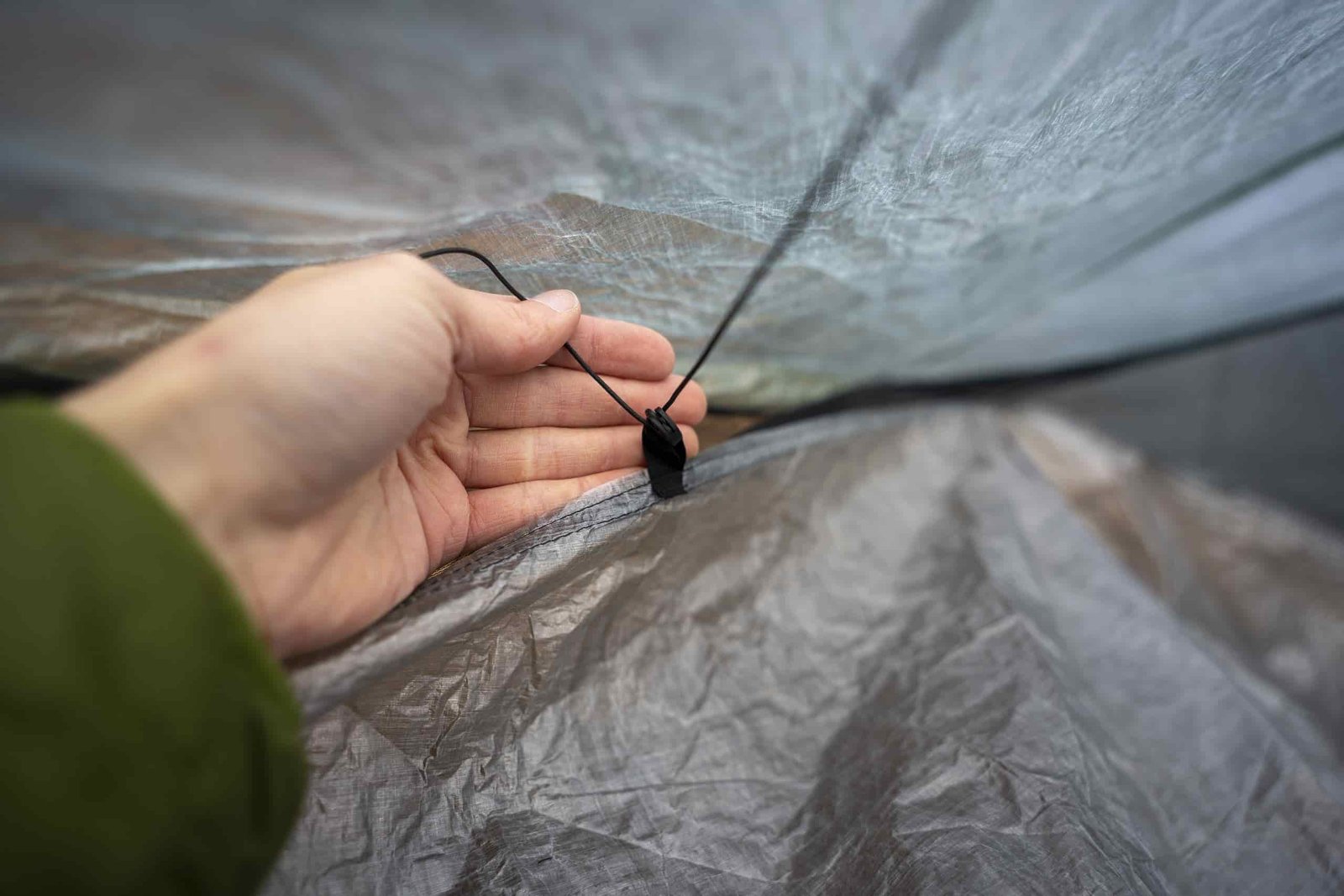 a hand holds a shock cord tensioning system on the interior of a tent