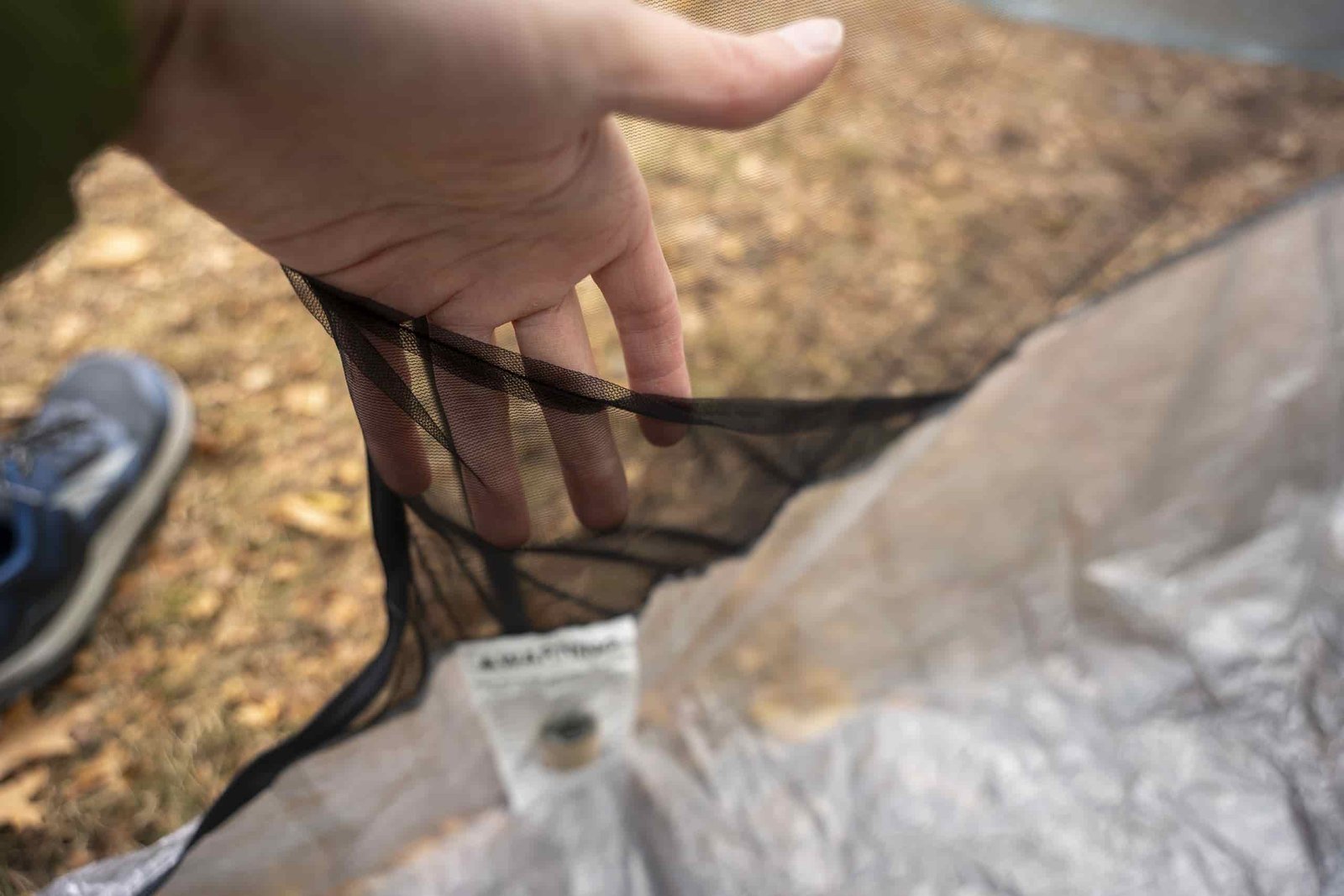 a hand holds open a triangular mesh pocket on the inside of a tent