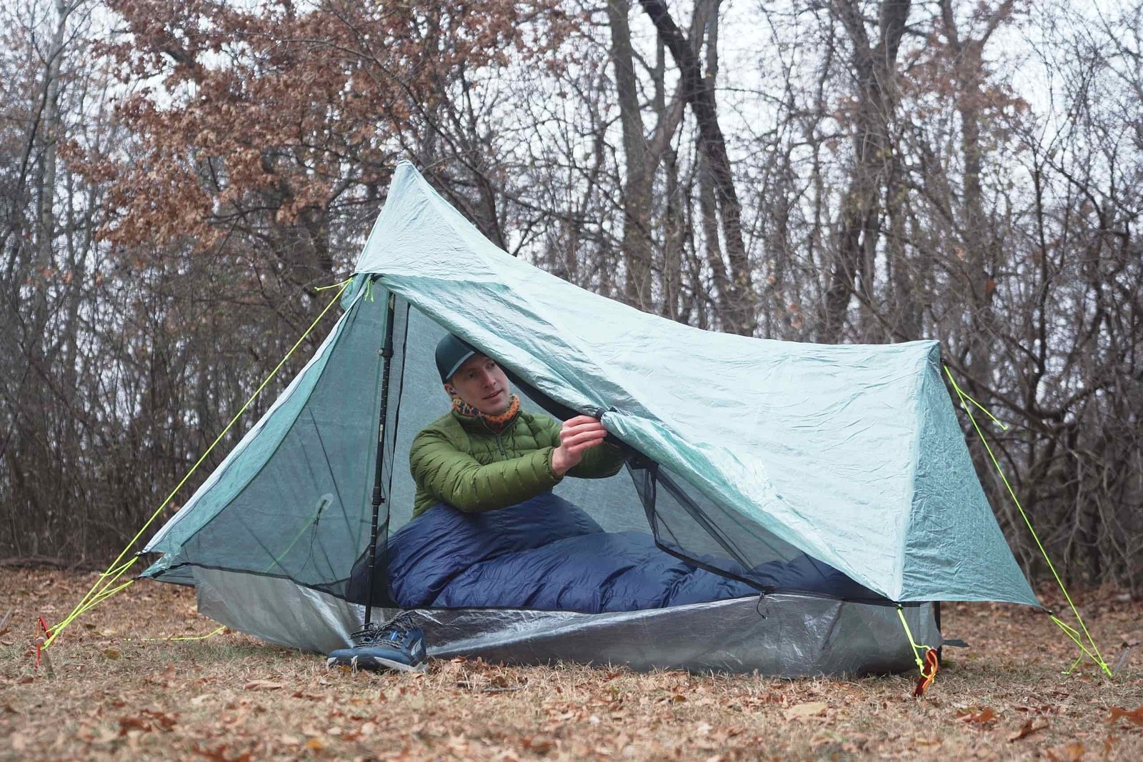 a man in a green coat sits in a one person tent