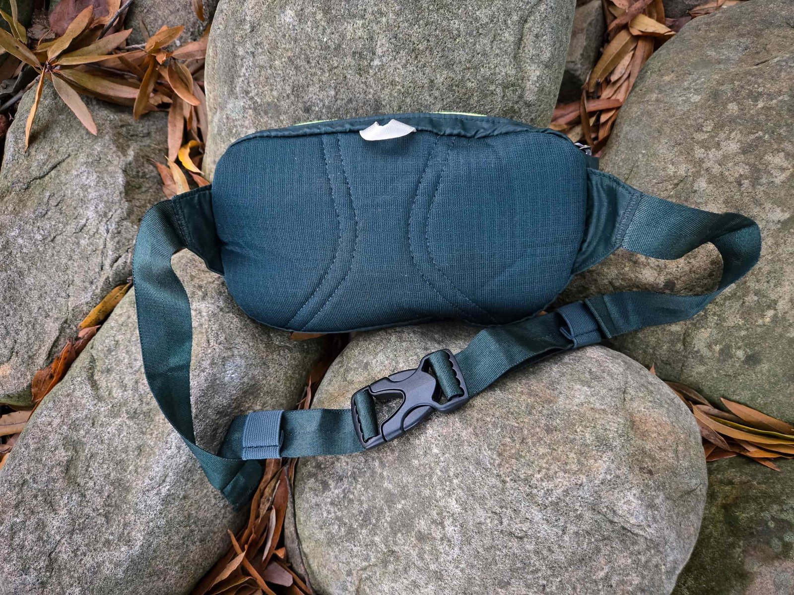 the padded back of the patagonia black hole mini hip pack resting on river rocks