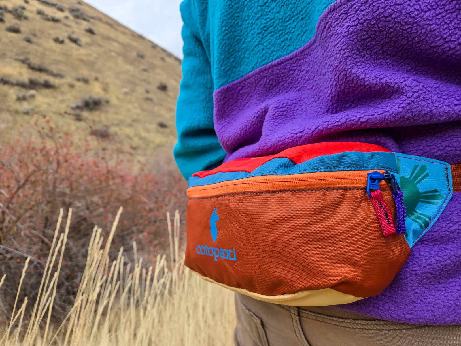 a zipped up cotopaxi bataan del dia resting on the lumbar of a man on a hike