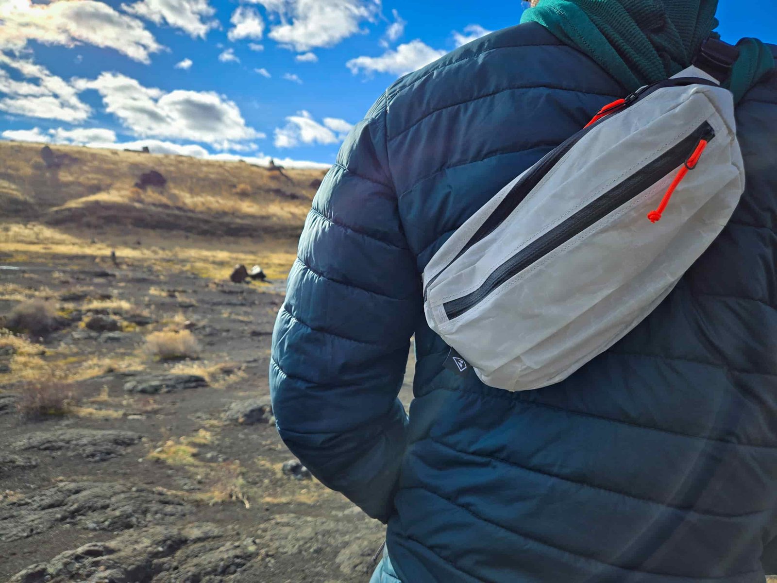 a man wearing the hyperlite mountain gear versa fanny pack slung over his shoulder while on a sunny desert hike