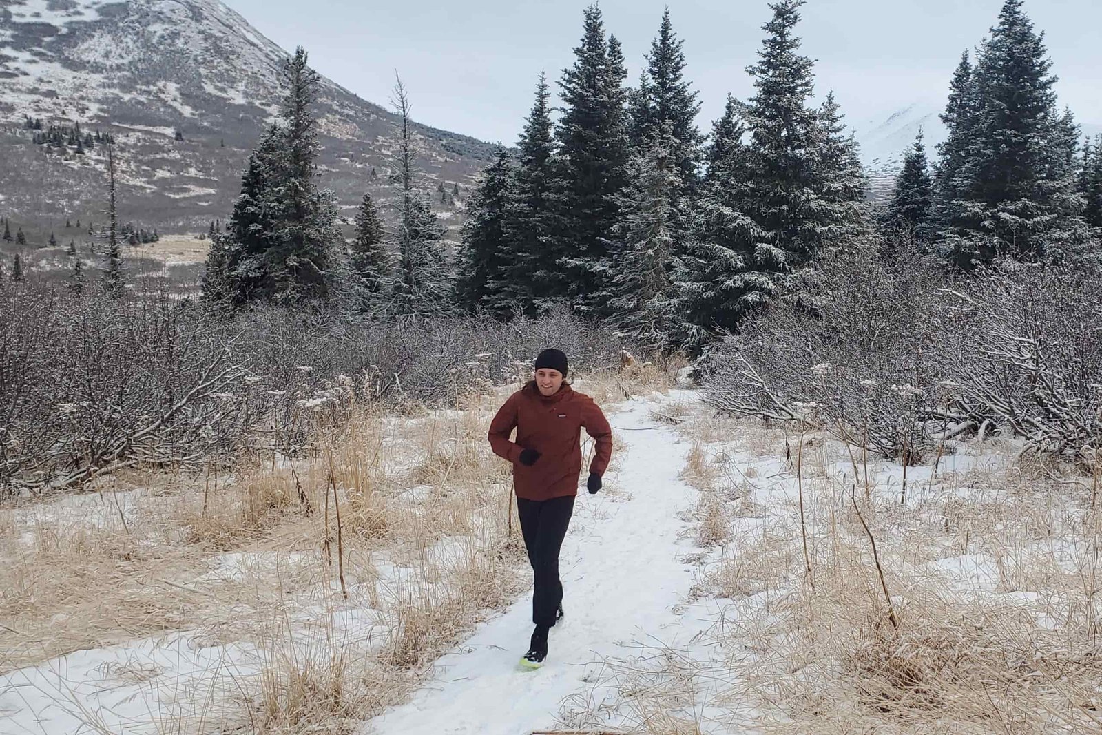 A man runs along a snow covered trail with mountains in the background.