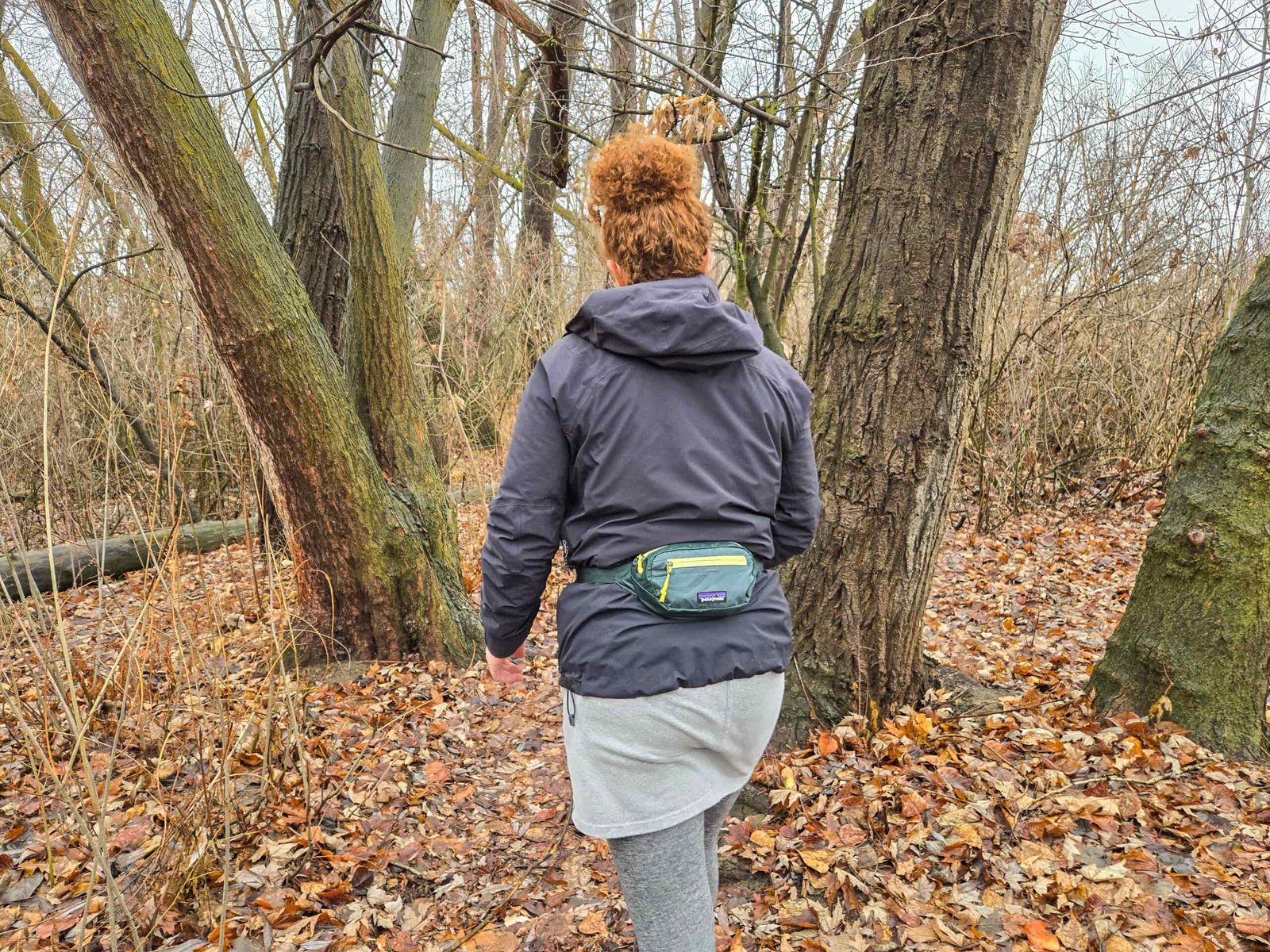 the view of the back of a woman hiking in the woods wearing a patagonia black hole mini hip pack on her lumbar