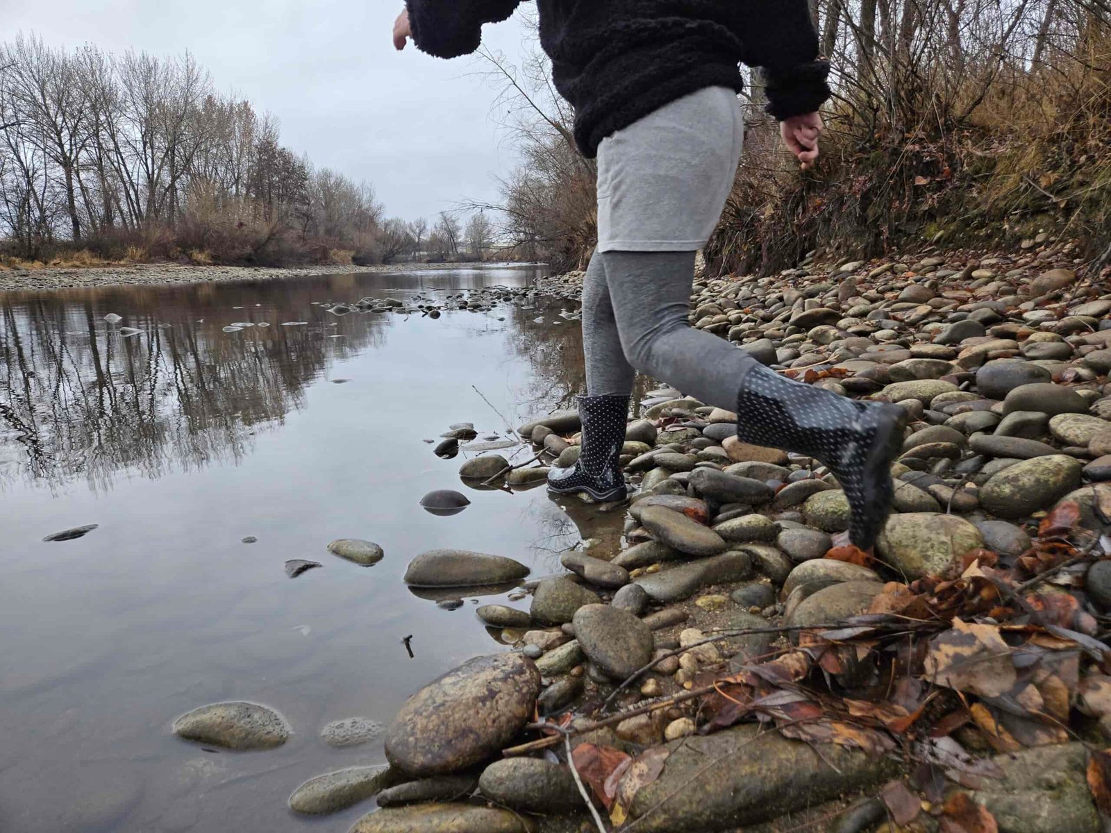 a woman wearing the sloggers rain and garden boot next to a still river with river rock on the edge