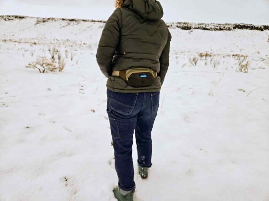 woman walking in snowy field wearing the kavu spectator fanny pack