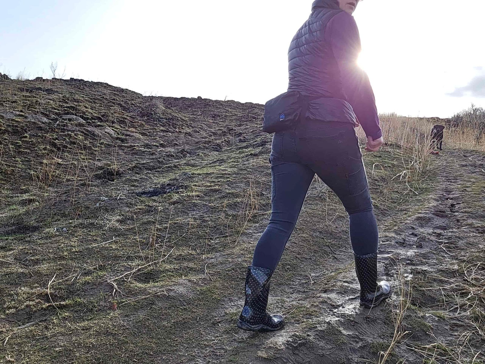 woman walking up a muddy trail with her dog at sunset