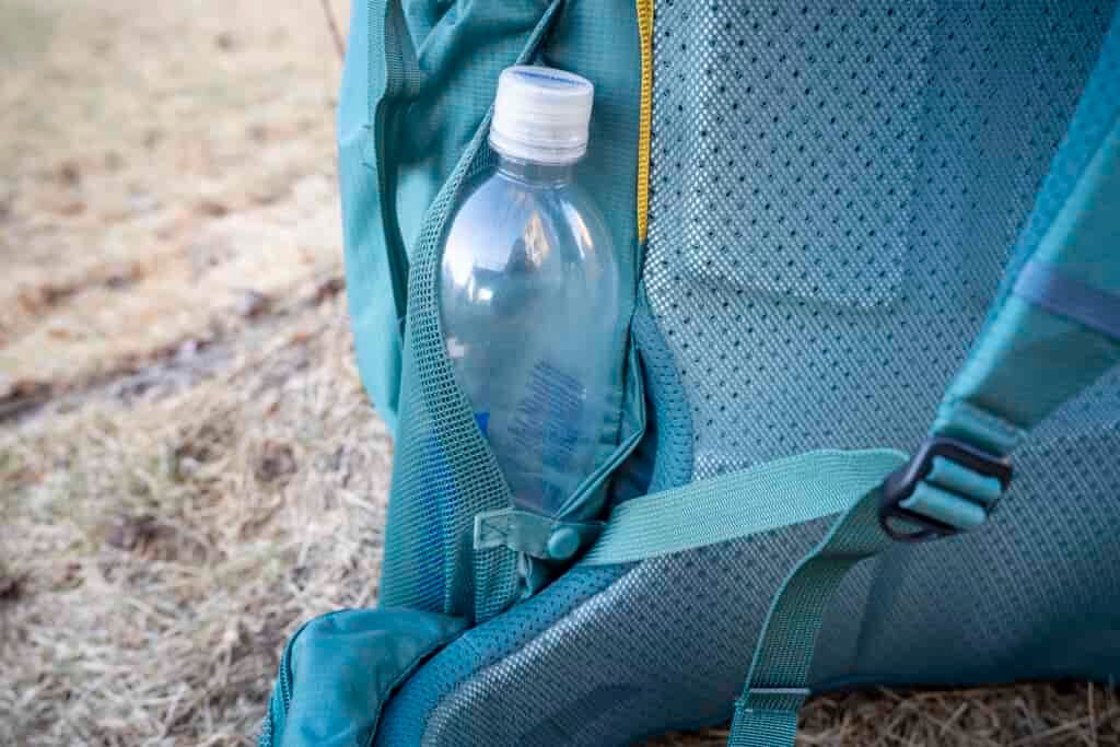 a water bottle rests in a pocket on the side of a backpack